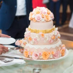 Bride and groom cut delicious wedding cake decorated with beige and pink roses