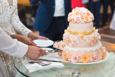Bride and groom cut delicious wedding cake decorated with beige and pink roses